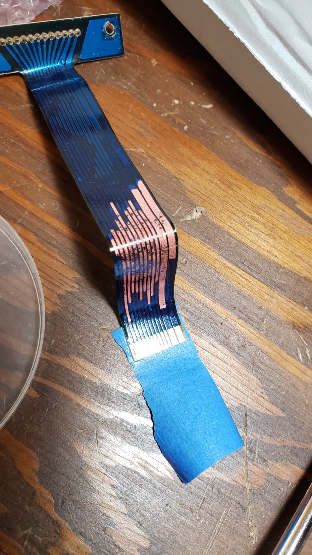 A flexible ribbon cable with visibly damaged copper conductors due to a leaking laptop battery.
